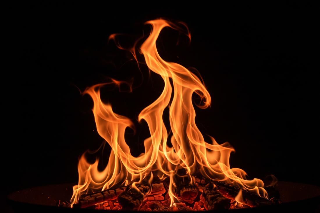Dramatic orange flames rising dfrom a fire pit against a dark background, symbolizing warmth, connection, and luxury outdoor living