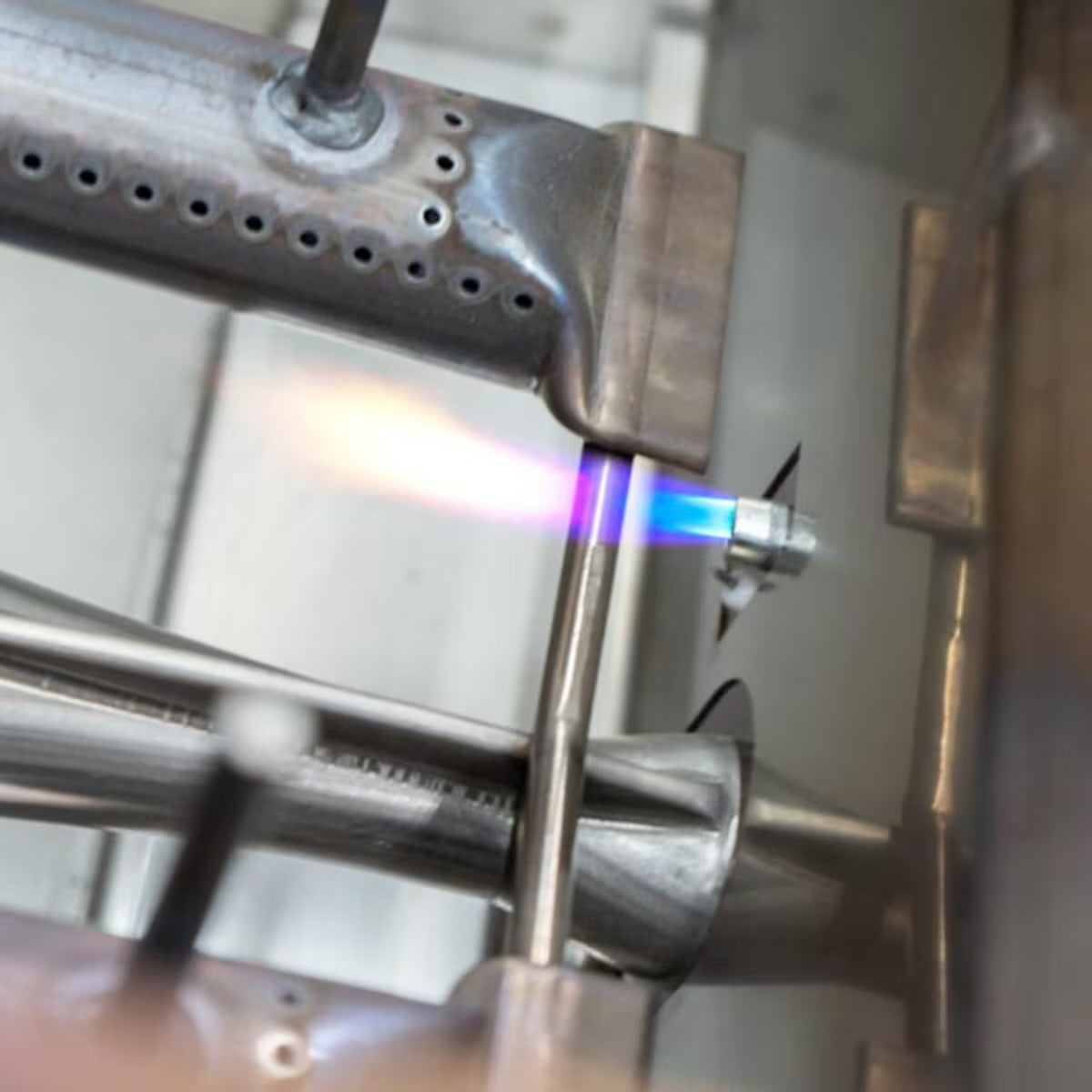 AOG built-in grill ignition burner tube with drilled flame ports, shown being lit with a torch flame during testing.