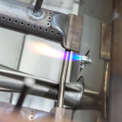 AOG built-in grill ignition burner tube with drilled flame ports, shown being lit with a torch flame during testing.