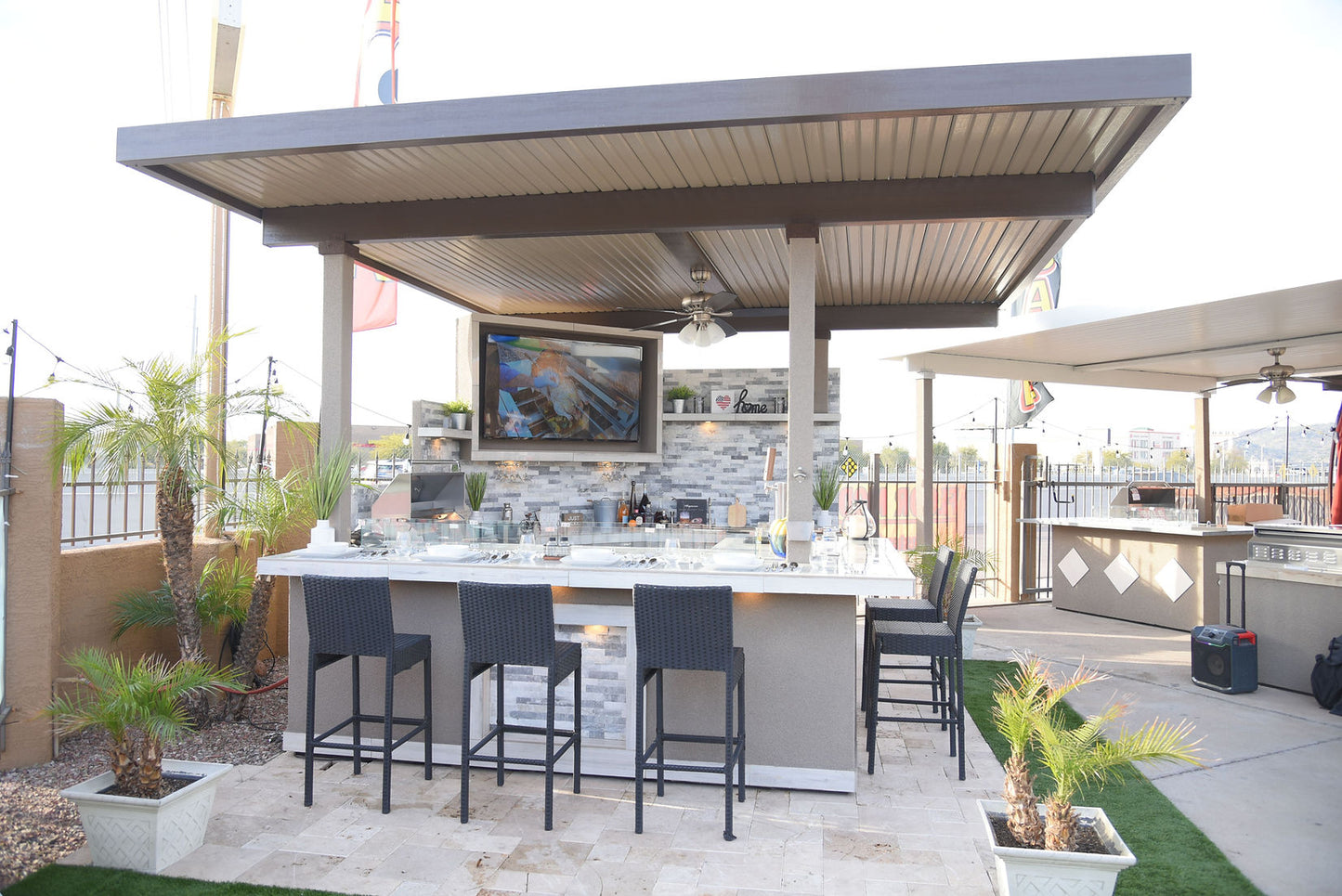 Outdoor kitchen with bar stools and a TV screen on a patio