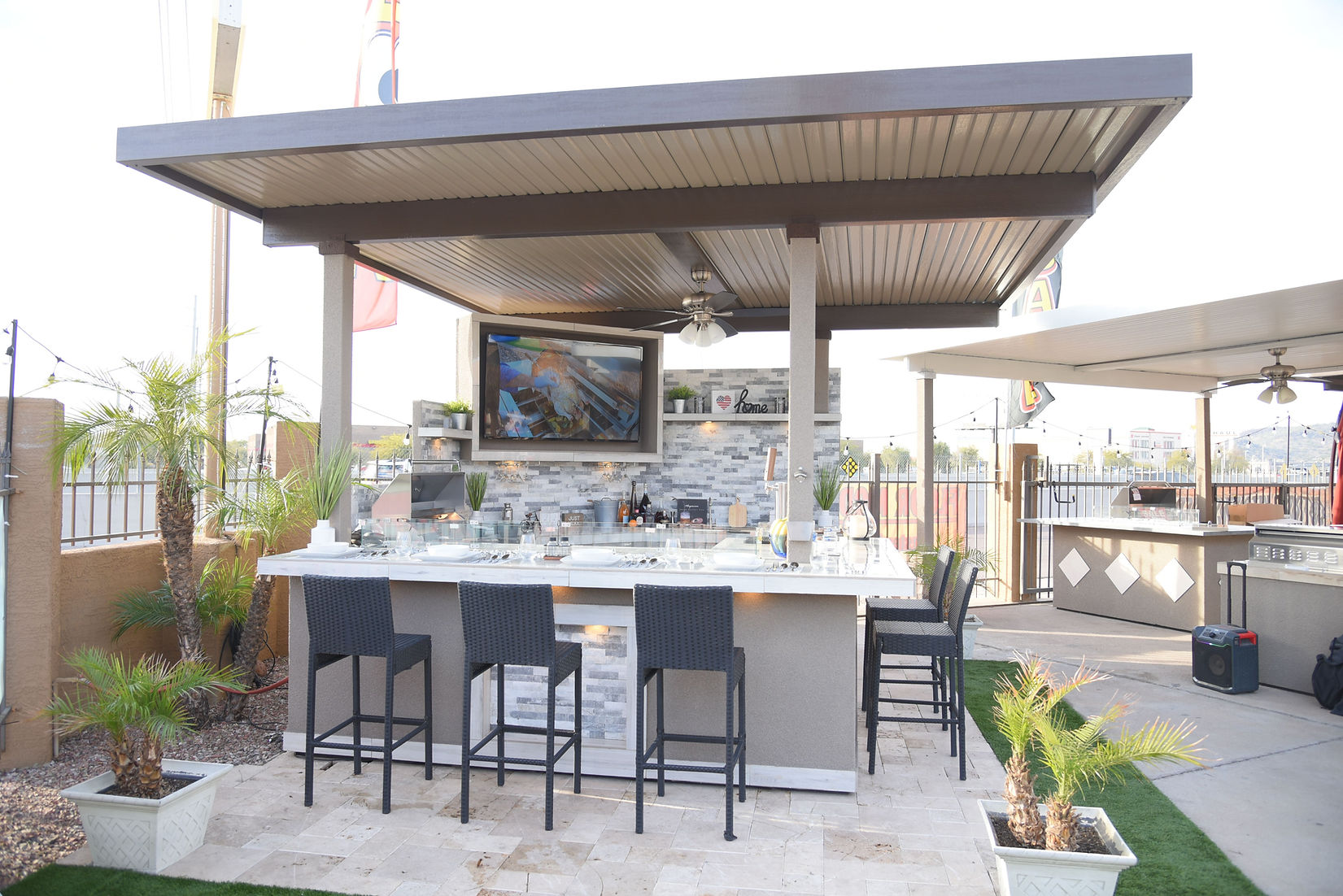 Outdoor kitchen with bar stools and a TV screen on a patio