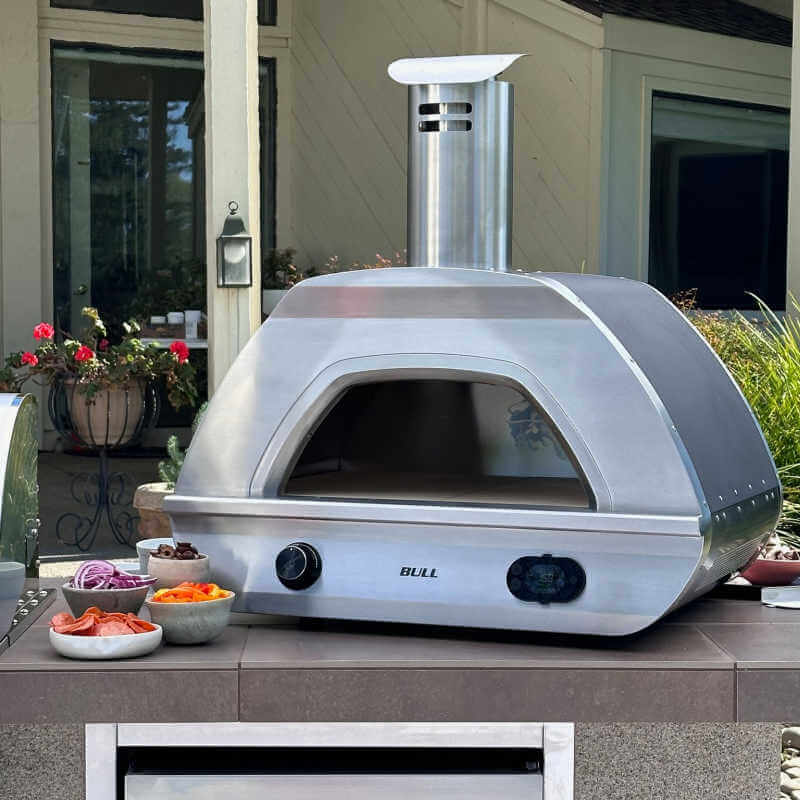Bull Dual Fuel Pizza Oven installed in outdoor kitchen countertop setup, shown with fresh pizza topping ingredients