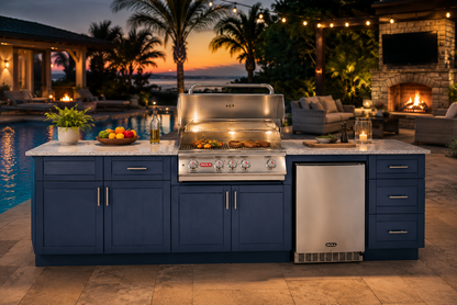 Luxury Bull outdoor kitchen island featuring an Angus 4-burner stainless steel grill, outdoor refrigerator, blue HDPE cabinetry, and granite countertops beside a resort-style pool and fireplace at sunset.