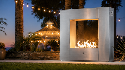 Modern stainless steel Williams outdoor fireplace with illuminated flames in a luxury backyard setting featuring palm trees, string lighting, and contemporary resort-style outdoor ambiance.