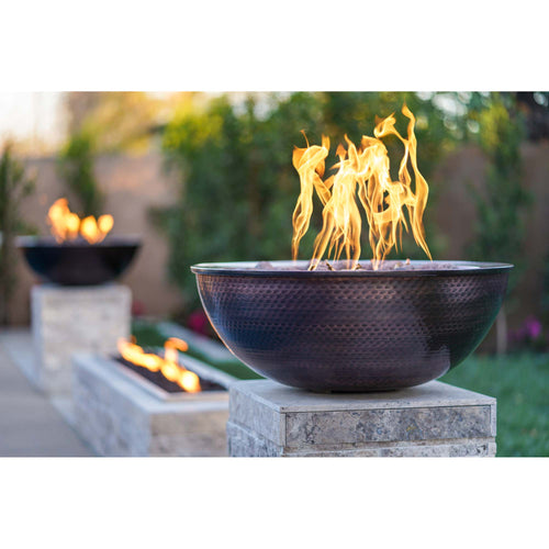Sedona 27-inch hammered patina copper fire bowl on stone pedestal with active flames, luxury outdoor fire feature for sophisticated entertaining