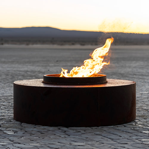 The Orbit circular smokeless fire pit with active flame on cracked ground, modern outdoor fire feature for contemporary patio entertaining