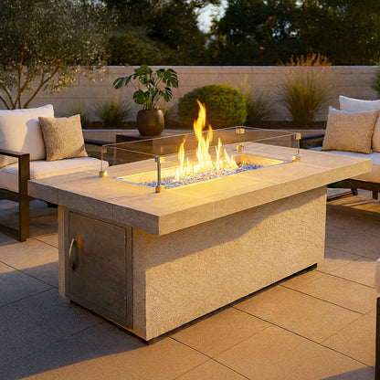 Luxury outdoor patio featuring the Cal Flame Phoenix RT501M rectangular fire pit table with glass wind guard, modern cushioned seating, warm evening lighting, porcelain tile top, and contemporary backyard entertaining atmosphere.