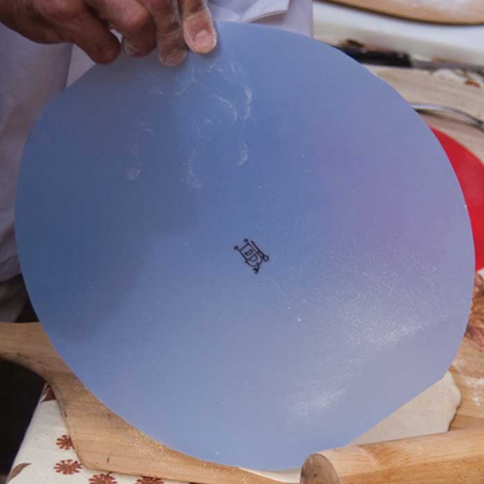 Non-stick dough rolling sheet in use, flattening pizza dough evenly on a countertop.