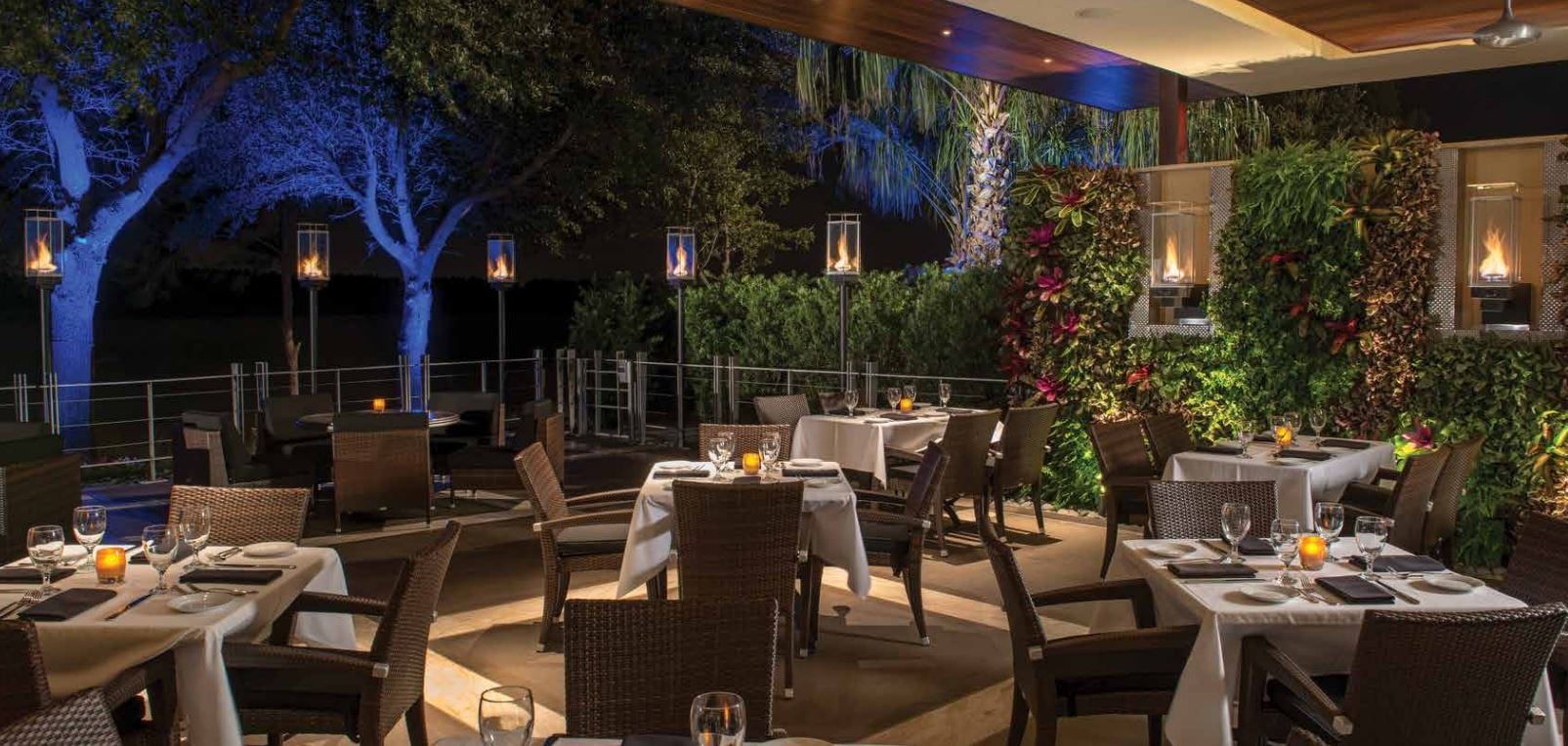 Tempest Torch Series illuminating a luxury outdoor dining patio with modern vertical flame torches, contemporary landscaping, and ambient nighttime architectural lighting.