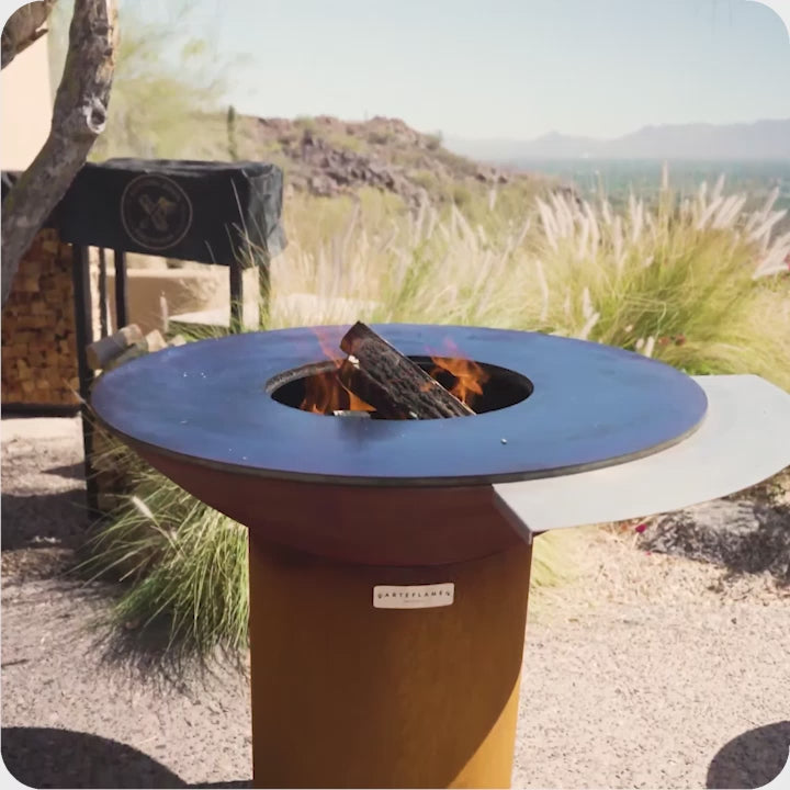 ArteFlame round corten steel fire bowl with live wood fire in a luxury desert outdoor setting
